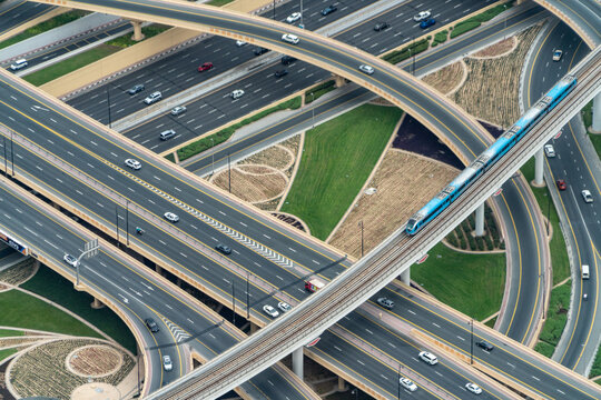 View of a complex multi-level highway interchange with a blue metro train and cars driving on ramps surrounded by green landscaping in Dubai, Dubai, United Arab Emirates.