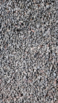 Top view of a textured surface featuring small, gray crushed gravel stones and pebbles, ideal for use as a natural background or construction material texture.
