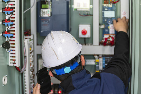 Service technician adjusting operational parameters inside electrical control cabinet of crew elevator system aboard commercial vessel.