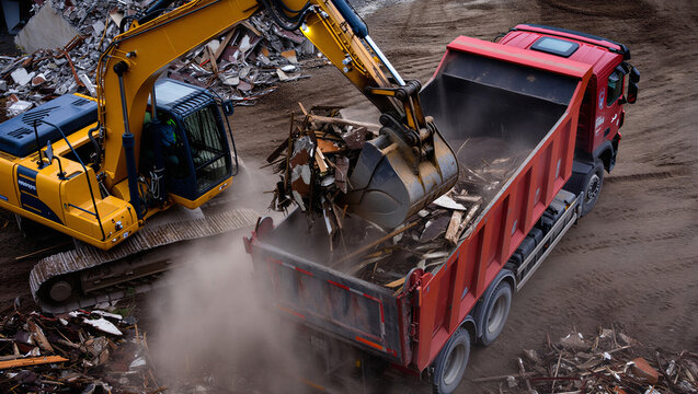 Excavator loading a dump truck with scrap metal or debris at an industrial construction site.