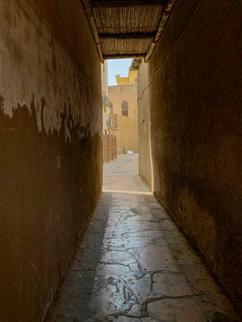 View of a traditional narrow alleyway in Al Fahidi with textured mud walls and stone-paved floor under a wooden ceiling in Dubai, Dubai, United Arab Emirates.