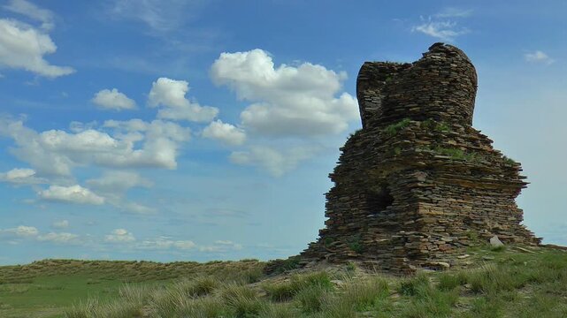 Ancient stupa in the Mongolian steppe on a background of blue cloudy sky.