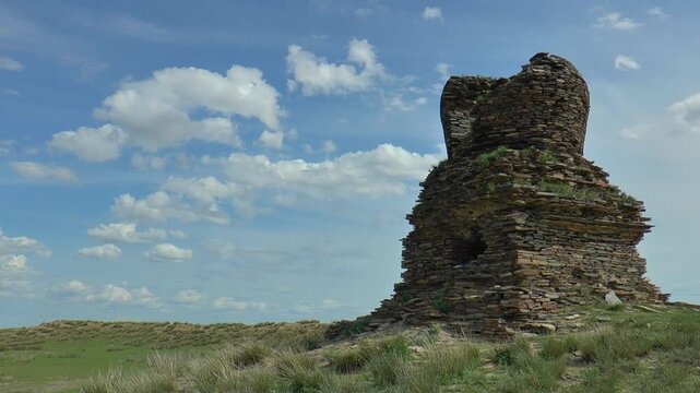 An ancient stupa in the Mongolian steppe against a blue cloudy sky, timelapse.
