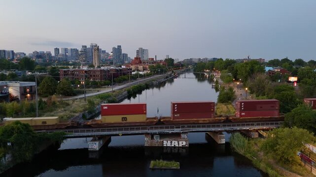Freight train crossing Lachine Canal at dusk with Montreal skyline and urban waterfront, Quebec, Canada. g.