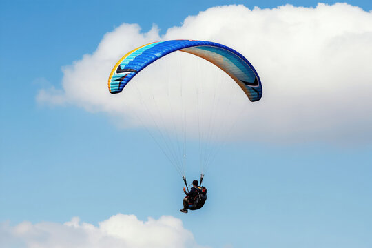 Person flies paramotor high blue sky. Colorful wing glides above white clouds. Solo man enjoys adventure activity, pure freedom, active hobby.