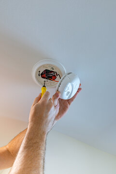 Electrician using a screwdriver to install a hardwired smoke and carbon monoxide detector to a ceiling junction box, USA