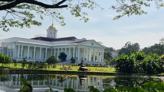 Morning view of Bogor Presidential Palace beyond a lotus pond, with lily pads and soft water movement reflecting the white neoclassical building.