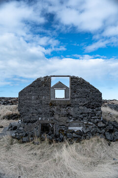 View of abandoned farmhouse ruins with empty window frames and stone walls under a cloudy blue sky Hafnarfjordur, Hafnarfjardarkaupstad, Iceland.