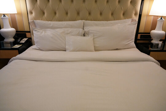 Clean white pillows and bed linens on a luxury hotel bed with a button-tufted headboard.Clean bedding and cozy hospitality accommodation concept with copy space.