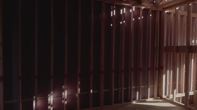Steady pan revealing wooden framing and staircase inside unfinished home.
