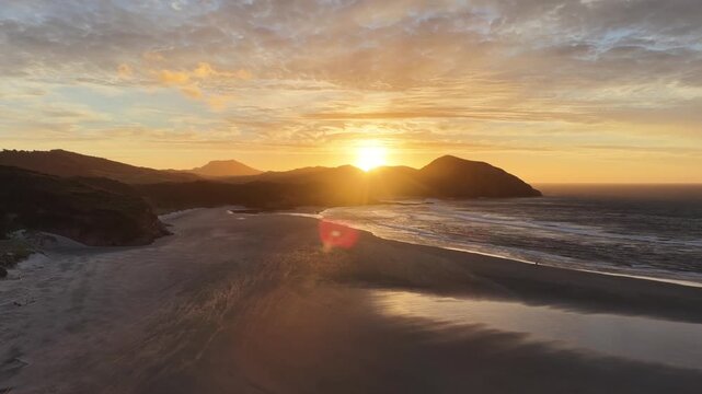 Aerial view of sunrise over remote sandy beach and rugged coastline, ocean waves visible