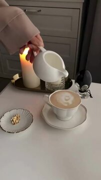 Pouring Milk Cream into Coffee Cup Creating Aesthetic Topping with Red Candle Background, Cozy Cafe Drink Concept