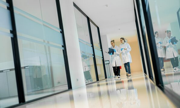 Two medical staff members walking in a hospital corridor while discussing patient care and daily tasks