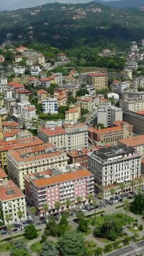 Vertical video. La Spezia, Italy. Aerial flight along Viale Italia embankment, terracotta rooftops, deep-water harbor with a large cruise ship docked under clear summer skies.. Drone footage. Rich co