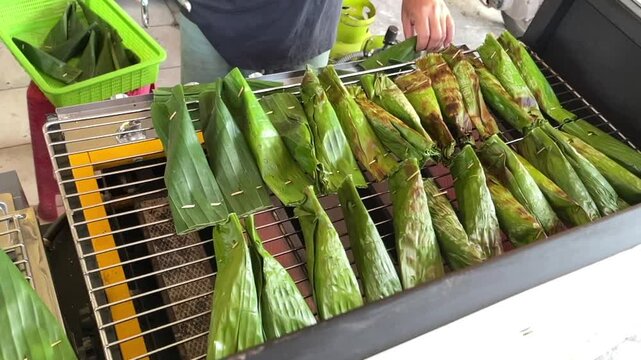 Otak-otak jumbo wrapped in banana leaves grilled on a charcoal rack by street vendor in Palembang, Indonesia, ideal for food, culture, and traditional cuisine themes.