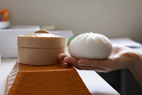 Close up of female hand holding a soft steamed bun shaped squishy toy beside a minimalist container. Anti stress object, sensory relaxation, anxiety relief and modern self care concept.