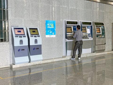 LIJIANG, CHINA - OCTOBER 25, 2017: A man using a CRH self-service ticket vending machine (TVM) inside a railway station in Lijiang, Yunnan province, featuring modern digital kiosks.