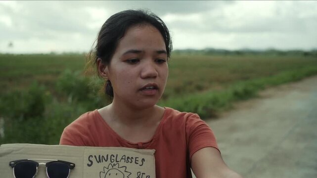 Impoverished Asian street vendor selling sunglasses on a rural road