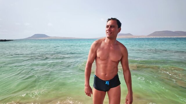 Muscular man walking out of the sea on Risco beach