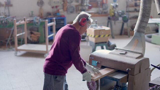 Senior carpenter sanding wooden plank in workshop