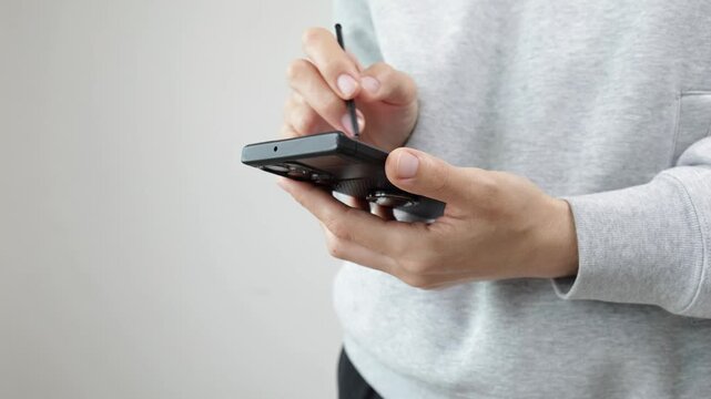 Hands using foldable smartphone with stylus on light background, touchscreen technology, mobile communication, modern digital device.