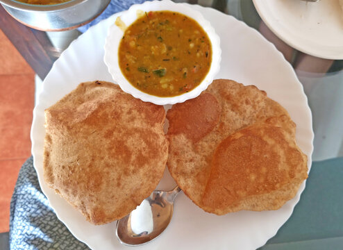 Crispy puffed pooris served alongside flavorful vegetable curry in white serving bowl.