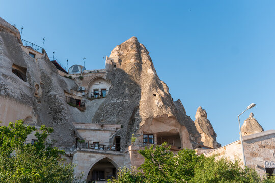 Goreme, Nevsehir, Turkey. Rock-cut cave dwellings carved into volcanic tuff formations, arched doorways and balconies integrated into fairy chimney spires under clear blue morning sky