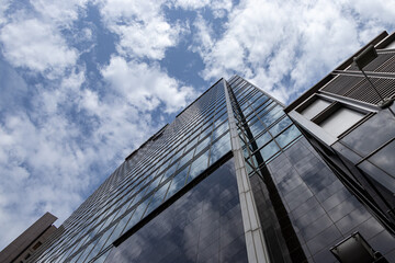 Fototapeta premium Modern glass skyscraper building reflecting blue sky and clouds business architecture