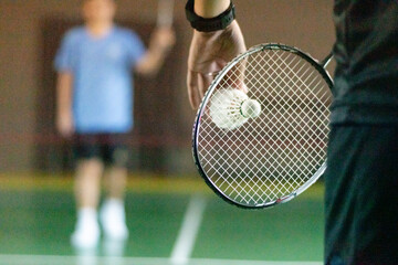 Badminton player holds racket and white cream shuttlecock in front of the net before serving it to another side of the court. © Sophon_Nawit