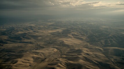 Naklejka premium Expansive arid terrain features undulating hills and distant fields, stretching to the horizon under a dramatic, cloudy sky, creating a feeling of desolation and remote wilderness