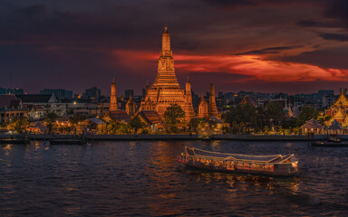 Obraz premium Majestic Wat Arun temple at sunset with golden sky over Chao Phraya River, Bangkok, Thailand.
