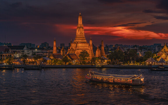 Majestic Wat Arun temple at sunset with golden sky over Chao Phraya River, Bangkok, Thailand.