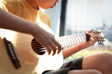 Focused young boy practicing acoustic guitar chords by the window with warm natural light. Concepts of education and the development of skills and creativity in music. © SUPERMAO