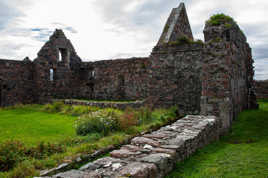 View of the historic stone ruins of Iona Nunnery with weathered walls and green grass under a cloudy sky in Baile Mor, Scotland, United Kingdom.
