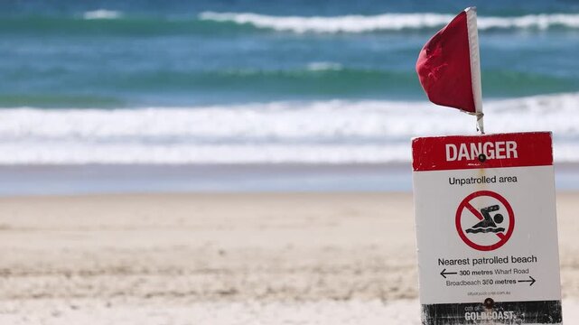 Red danger flag and warning sign on sandy beach with ocean waves in background at Gold Coast Australia.