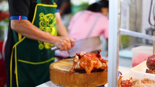 Street food chef carving roasted duck with cleaver on wooden board at asian night market.