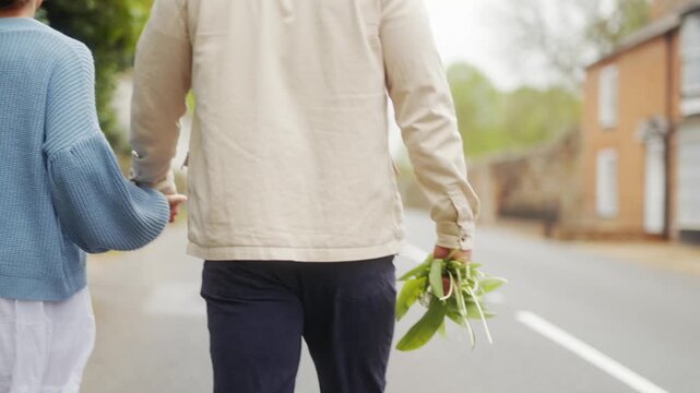 Couple holding hands carrying foraged greens while walking on a village road