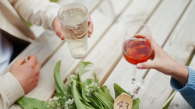 Two people enjoy drinks on a wooden table with wild garlic and flowers