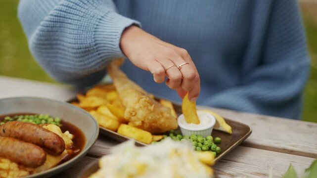 A close-up shot of a person dipping a golden chip into sauce outdoors