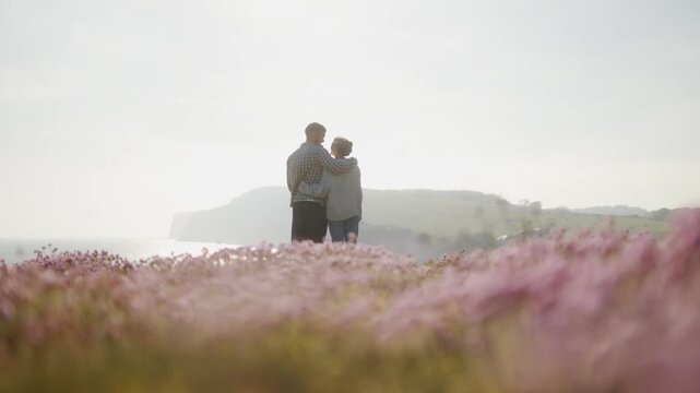 Couple embraces while looking out over hazy calm ocean from clifftop