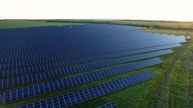 Aerial footage of clean energy facility at sunset, featuring long solar rows in countryside setting. Strong stock visual for utility infrastructure and sustainable future concepts