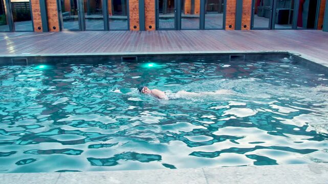 Female athlete swims front crawl in backyard pool with glowing underwater lights. Sport footage presents endurance training, body rotation, and streamlined movement