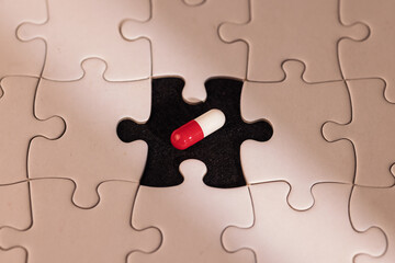 Fototapeta premium Detailed view of a white puzzle missing one piece with a glowing pill in the empty space under a light ray on a deep black backdrop.