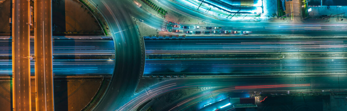 Aerial night view of modern highway interchange with dynamic light trails representing sustainable transportation, EV mobility, smart city growth, ESG investment, and futuristic urban infrastructure.