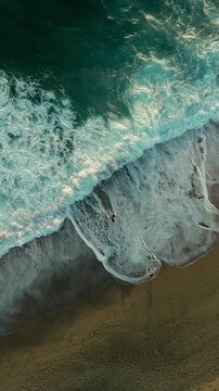 Aerial view of ocean waves crashing on a sandy beach.