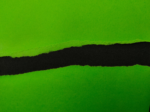 Two pieces of vibrant green paper are torn to reveal a dark, black textured space between them