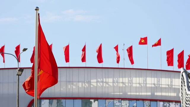 National flags of Vietnam waving in the wind against a blue sky. Row of red Vietnamese flags with a yellow star and communist party flags on a building roof. Patriotic and political stock footage.