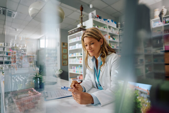 Smiling pharmacist reading medicine box label while working in drugstore.