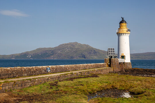 View of Tobermory Lighthouse standing at the end of a stone pier overlooking the sea and distant hills in Isle of Mull, Scotland, United Kingdom.