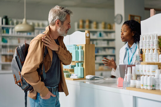 Mature man complaining of shoulder pain to his pharmacist in pharmacy.